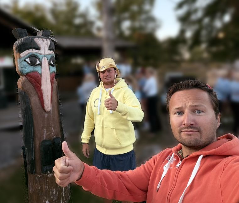 August på Oksnøen med tommelen opp, foran en utskåret totempæl